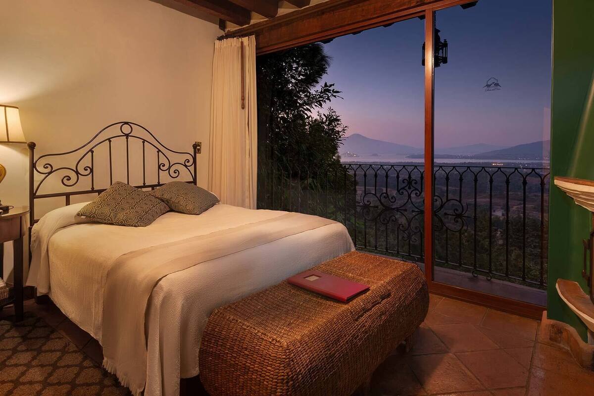 A bedroom with a bed, bedside lamp, and a view of the outdoors.