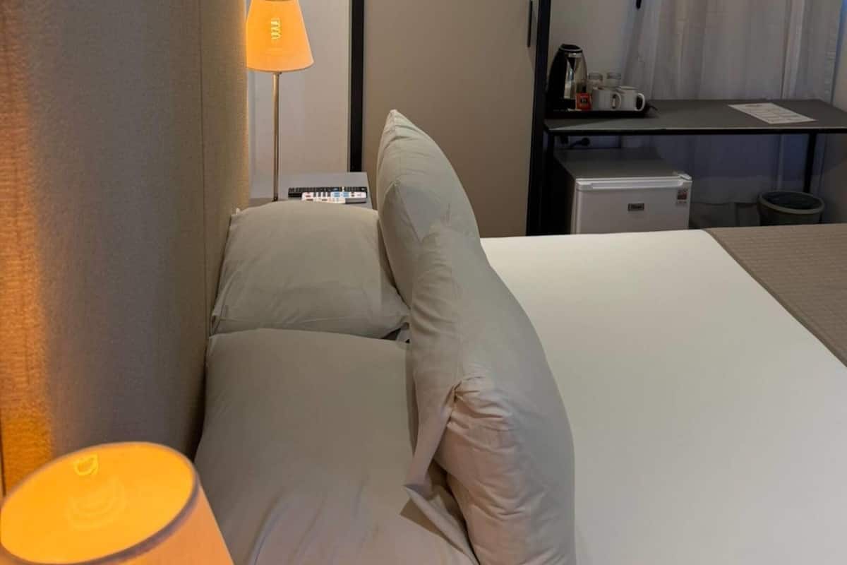 Een hotelkamer met een bed, een bureau met lamp, een koffiezetapparaat en een kleine koelkast.