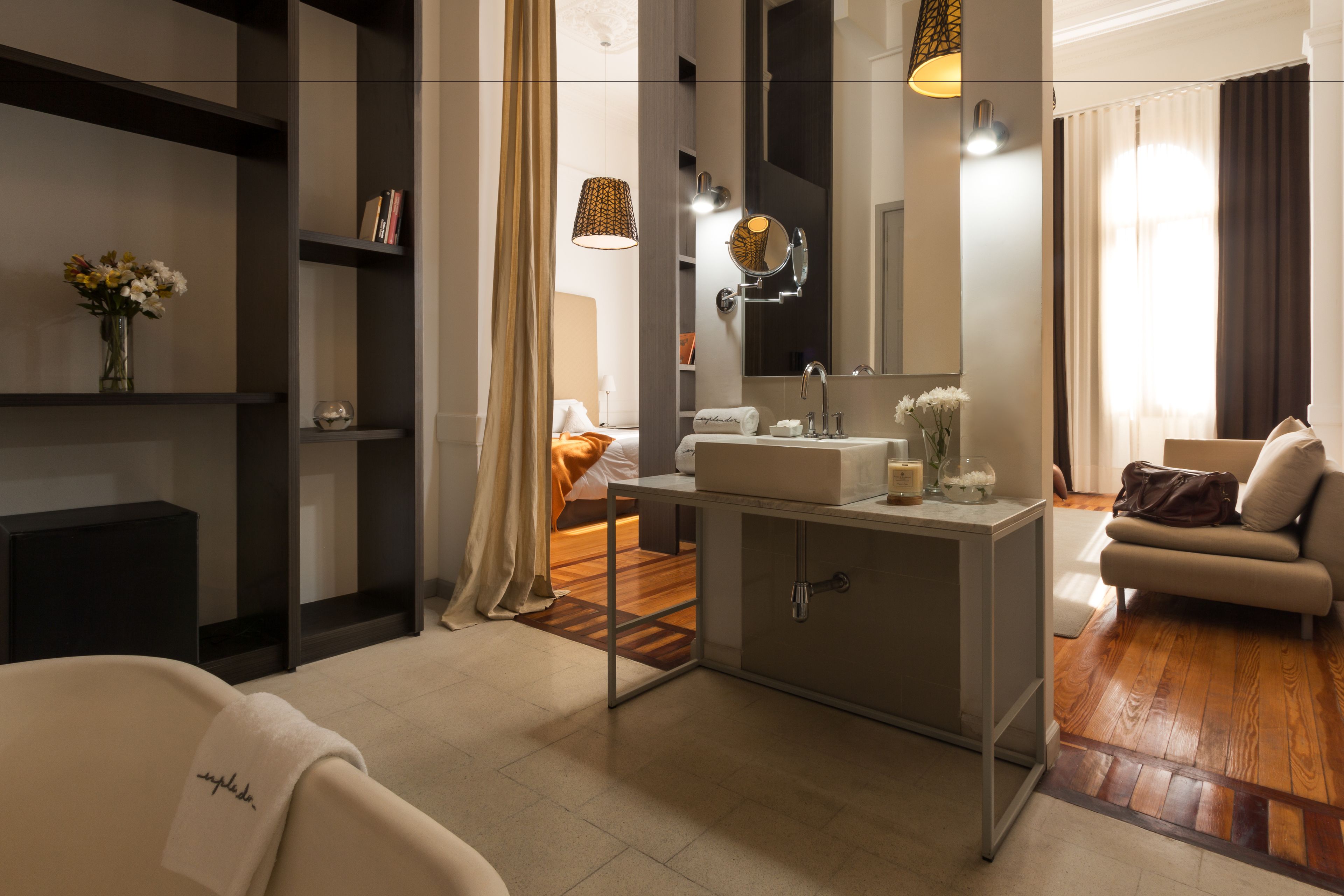 A modern hotel room with a large bed, a sofa, a vanity with a mirror, and a small table with toiletries.