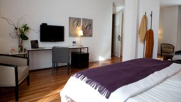 Una habitación de hotel con cama, escritorio, silla, televisor y obras de arte en la pared.