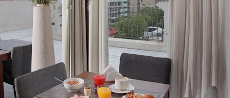Un comedor con una mesa dispuesta para el desayuno, un florero con flores y vistas a la ciudad.