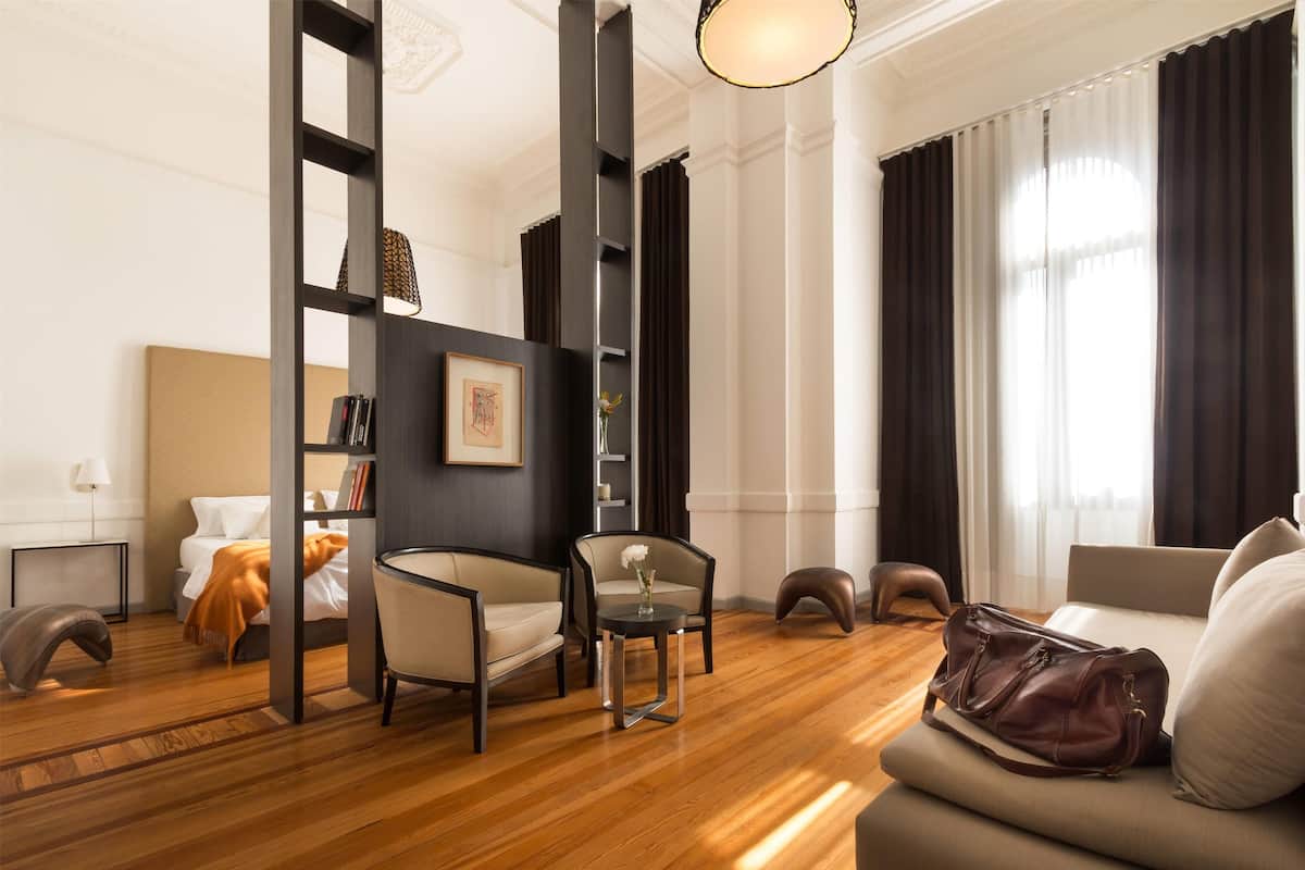 Een moderne hotelkamer met een houten vloer, een bank, een stoel, een klein tafeltje en een boekenplank.