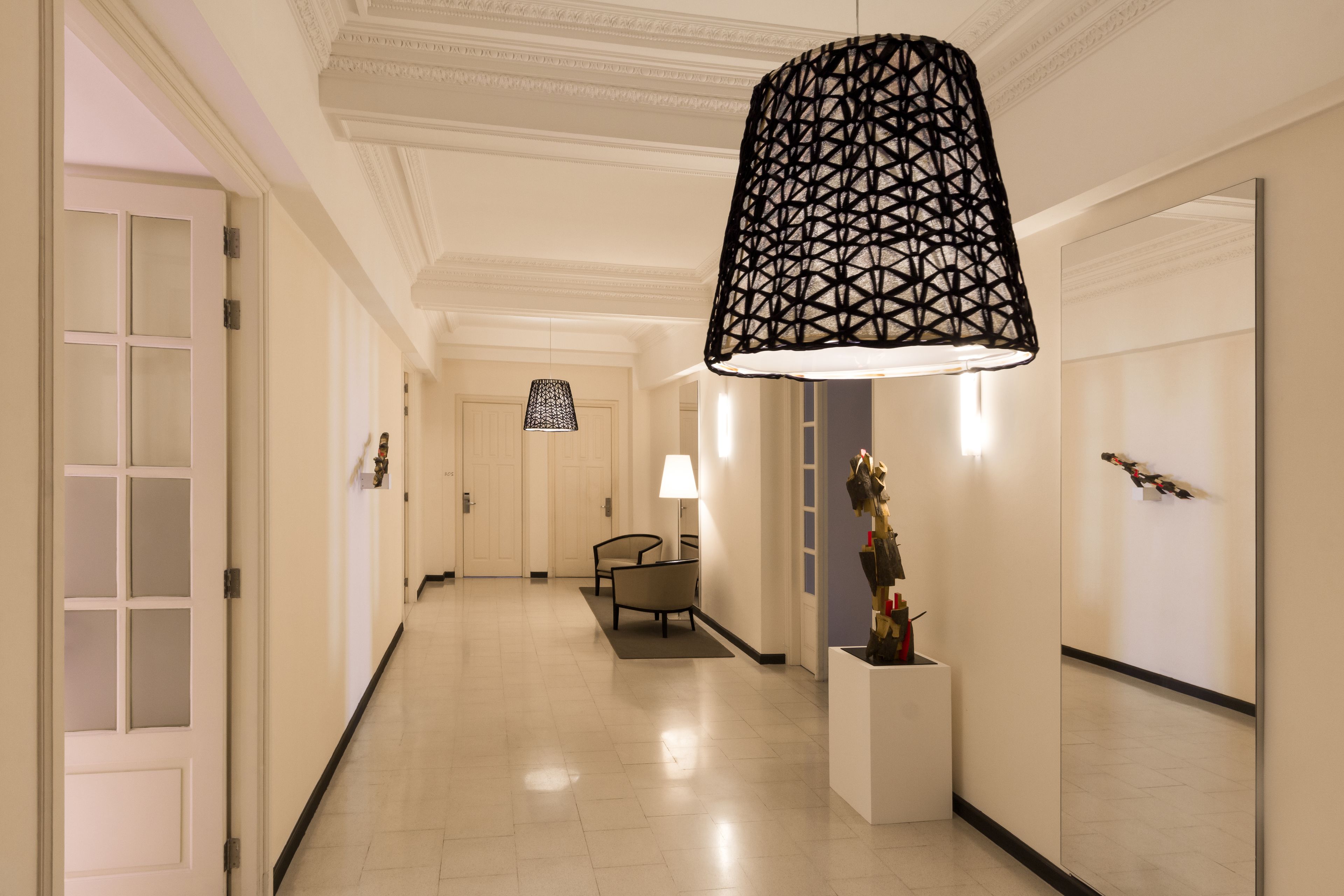 A hallway with a geometric pendant light, a mirror, and a small table with a lamp.