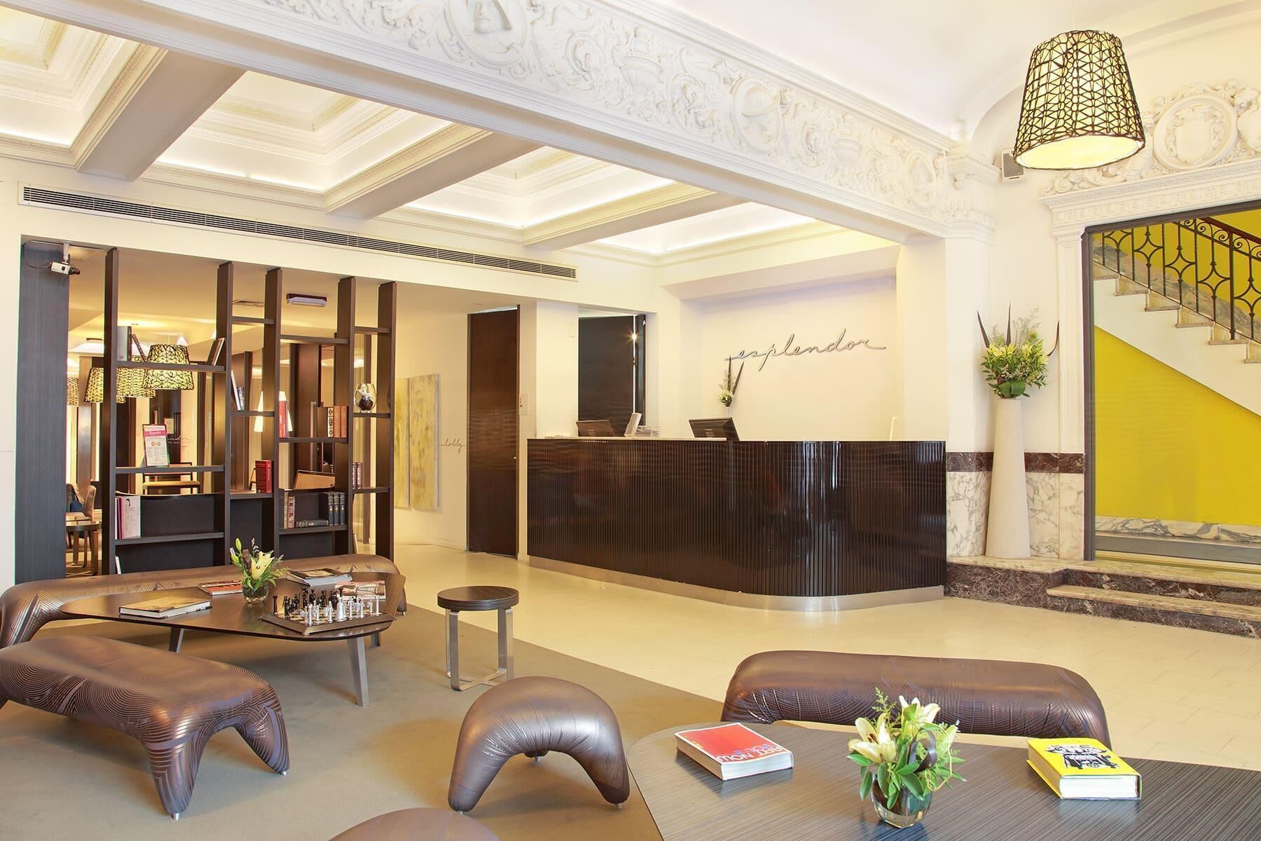 A hotel lobby with a reception desk, seating area, and a staircase.