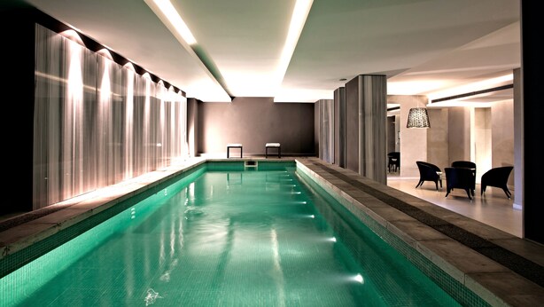 A swimming pool with a tiled edge, a ceiling with linear lighting, and a seating area with chairs. - Esplendor by Wyndham Montevideo Cervantes (Montevideo)