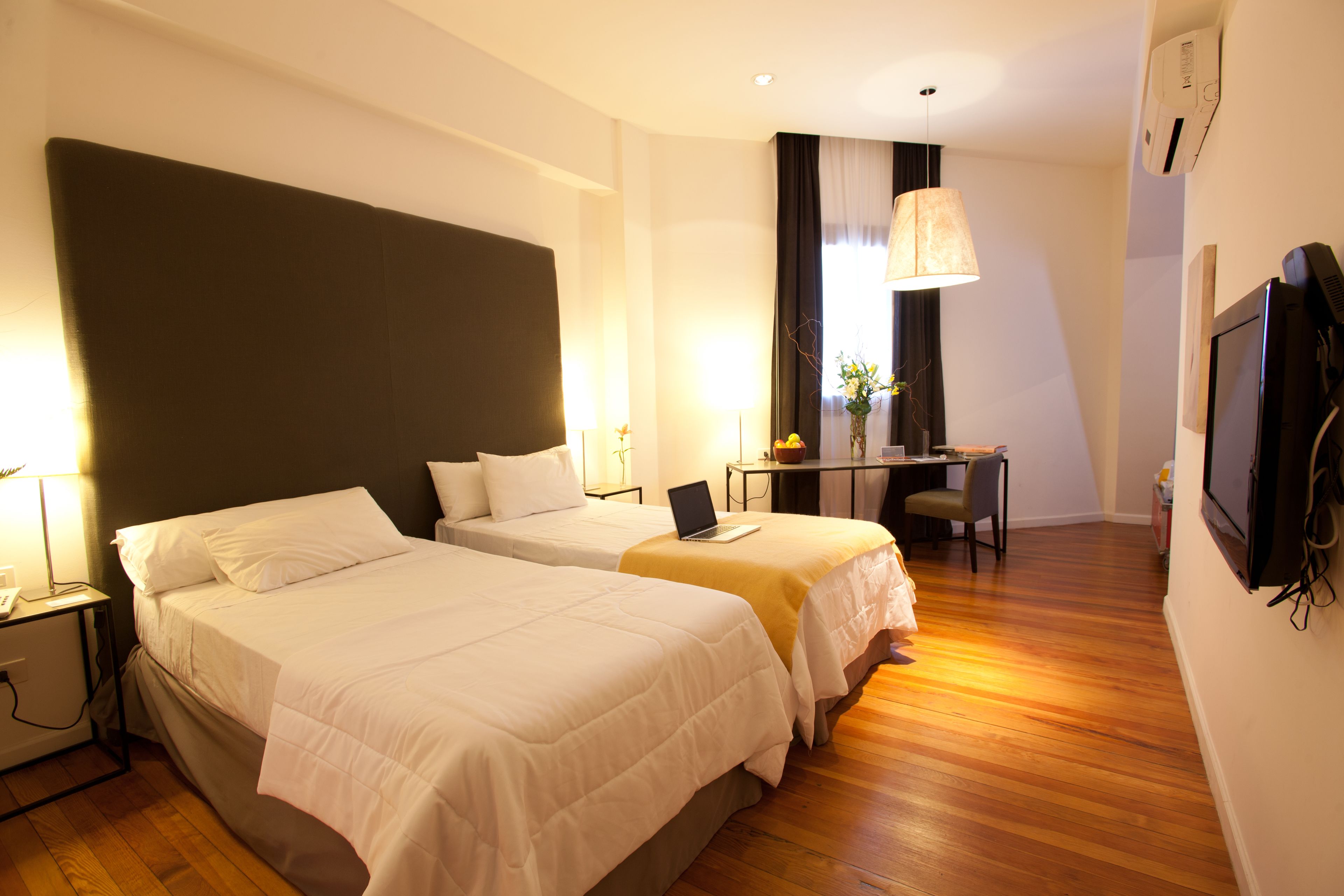 A hotel room with two beds, a desk, a chair, a TV, and a lamp.