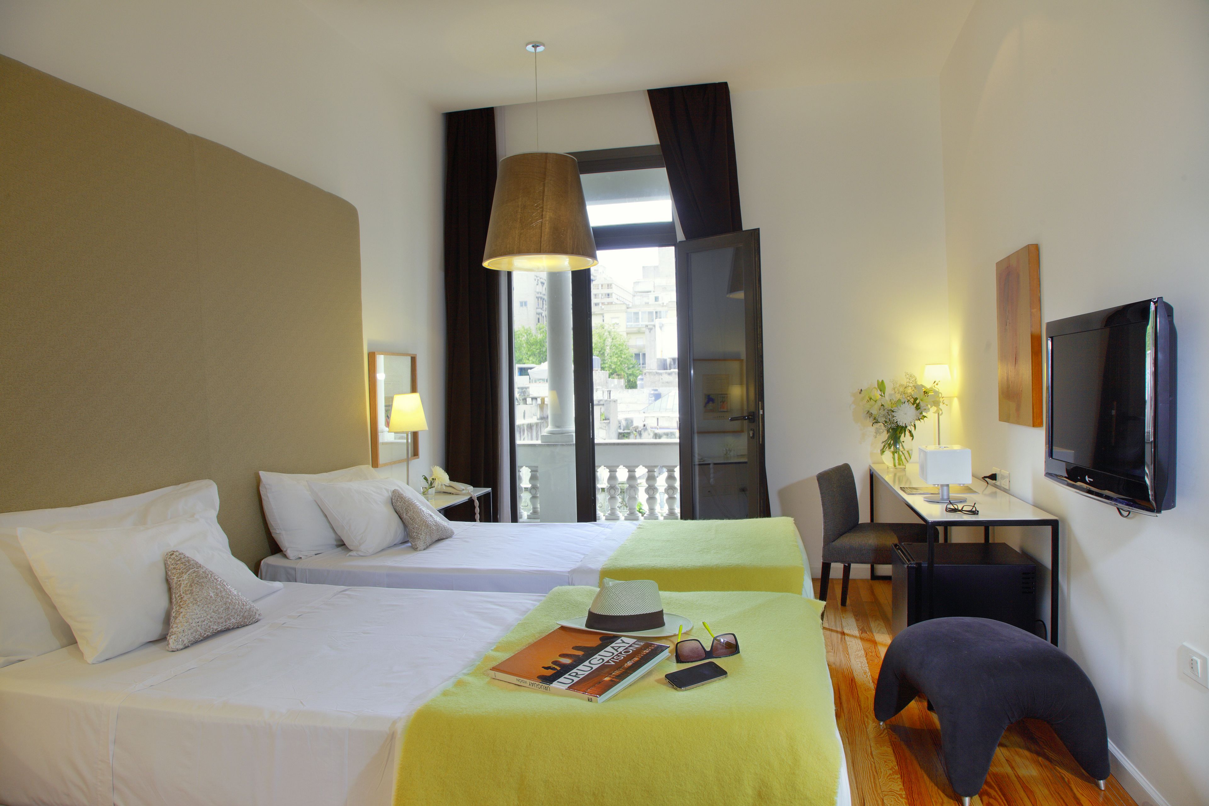 A hotel room with two beds, a desk, a chair, a television, and a window with a view of buildings.