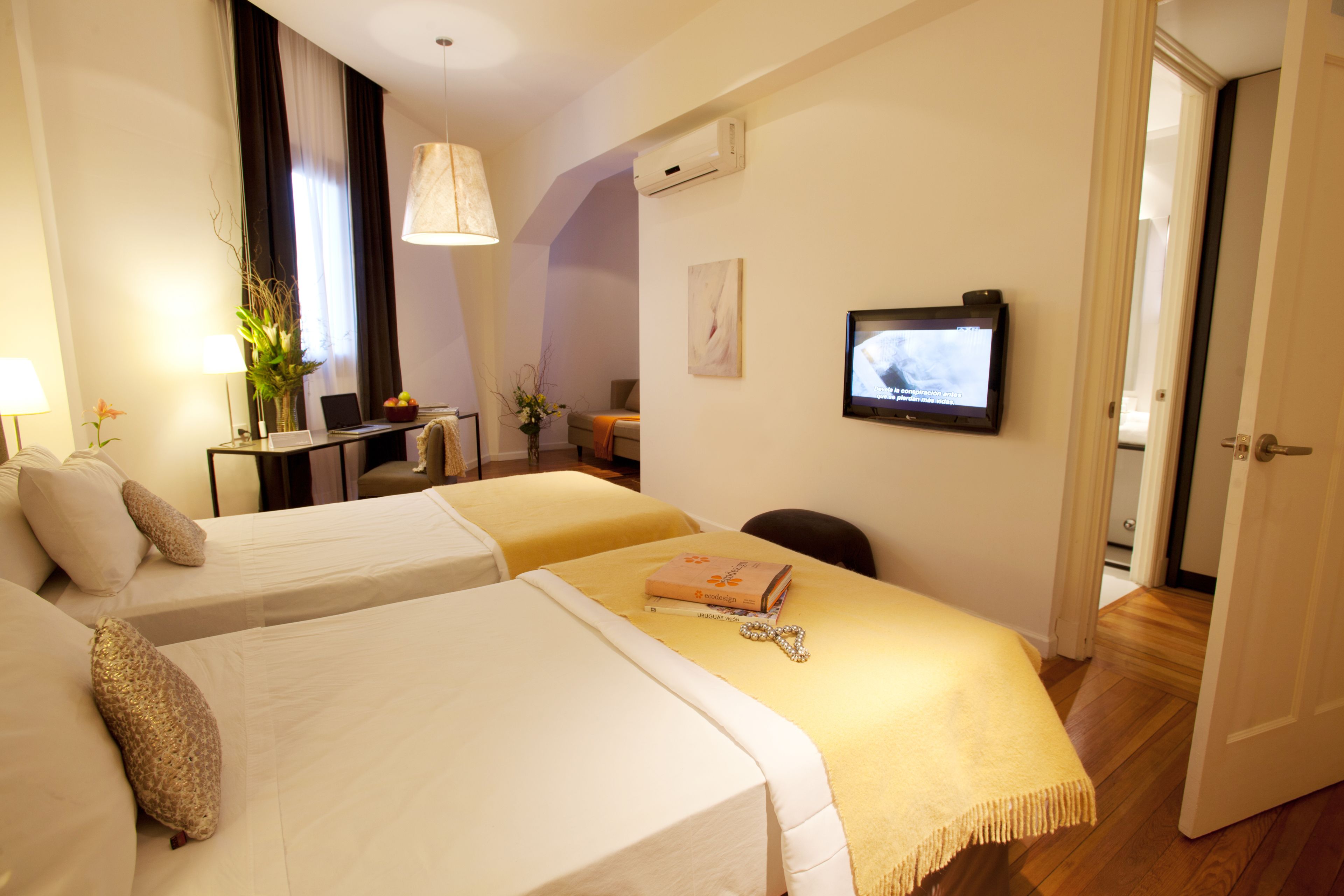 A hotel room with two beds, a desk, a chair, a television, and an open door leading to another room.
