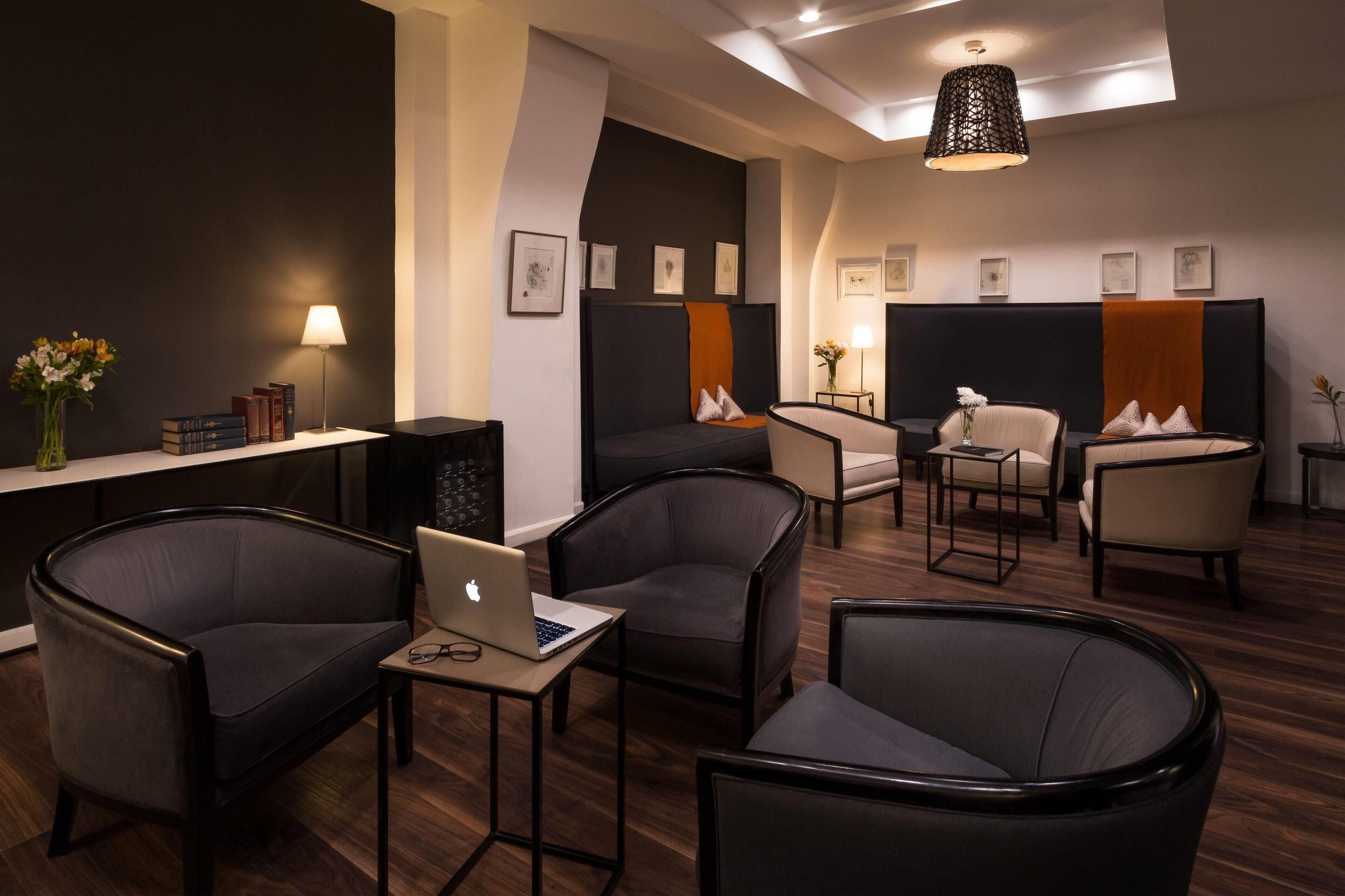 Een moderne hotellobby met donkere zithoeken, een receptiebalie en kunstwerken aan de muren.