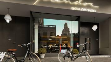 A hotel entrance with a neon sign, two bicycles parked in front, and a view of a historic building through the window.