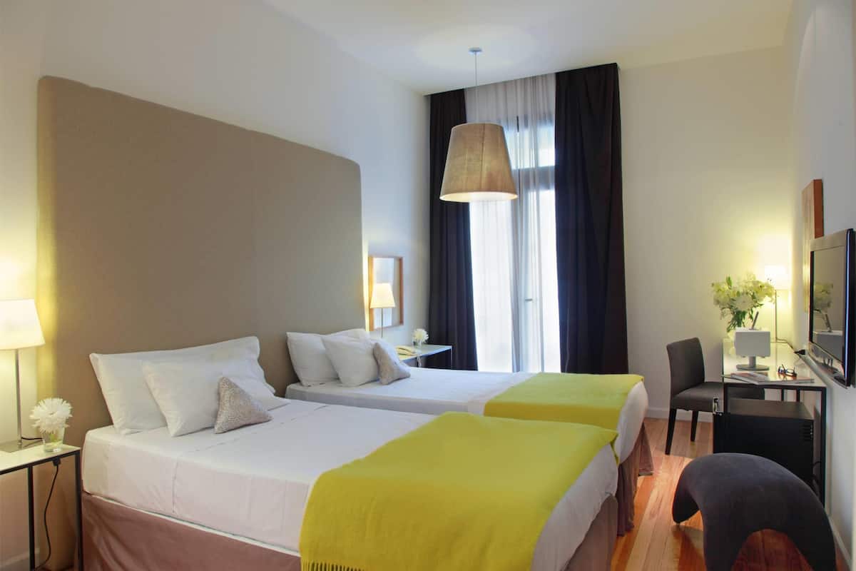 Hotelkamer met twee bedden, een bureau, een stoel, een televisie en een raam met gordijnen.