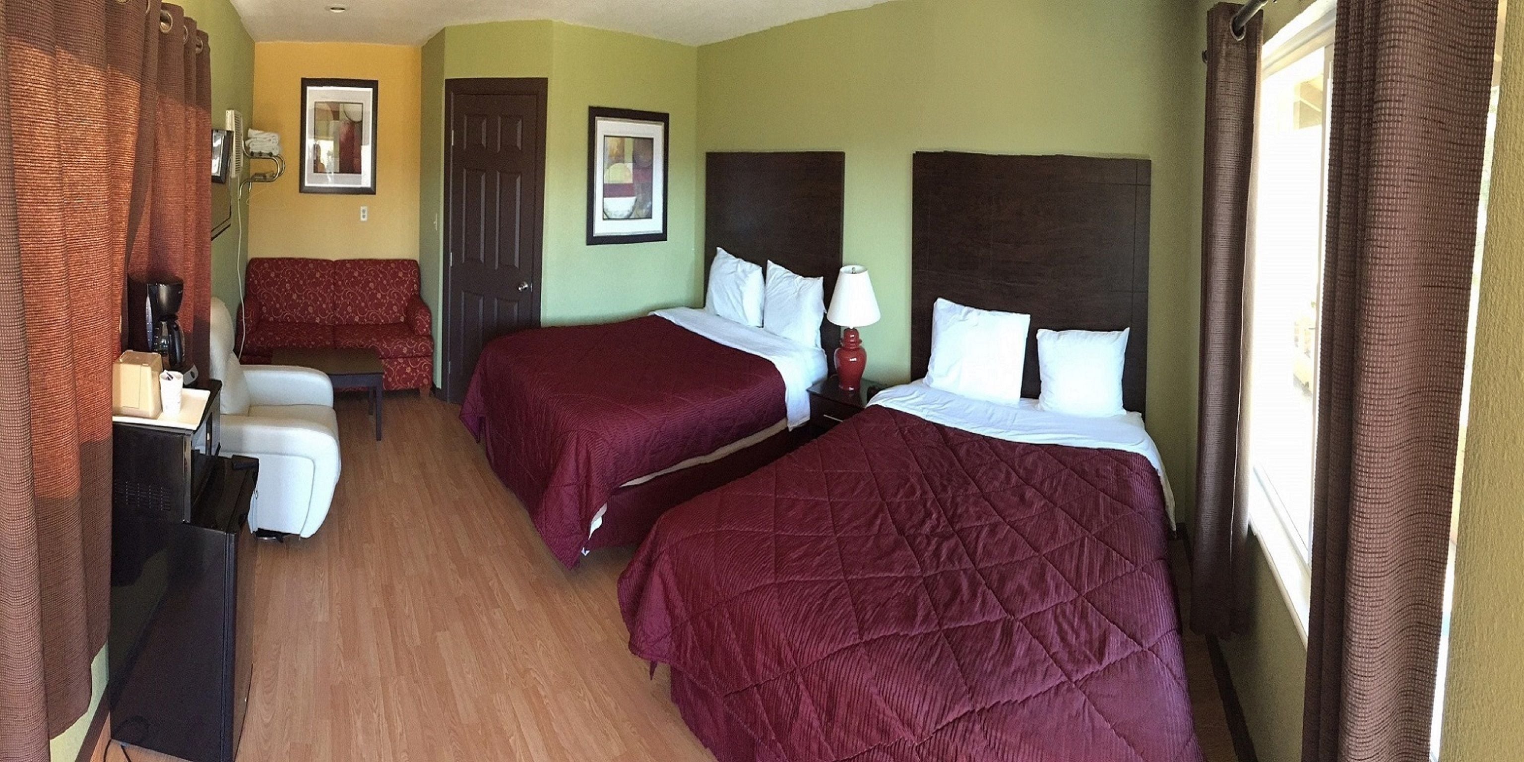A hotel room with two beds, a desk, a chair, and a window with curtains.