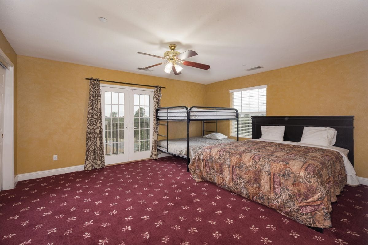 A bedroom with a bunk bed, a large bed, a ceiling fan, and a patterned carpet.