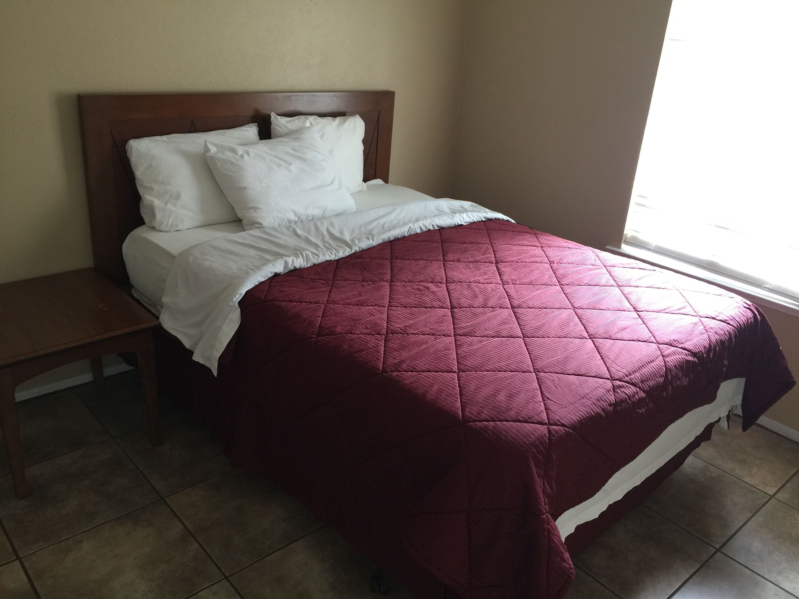 A bed with a wooden headboard, white bedding, and a red quilt.