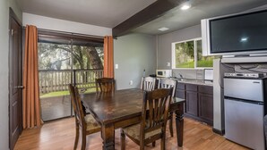 A kitchen with a dining table, chairs, a refrigerator, a microwave, and a television. - Mountain Trail Lodge & Vacation Rentals (Oakhurst)