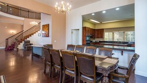 A spacious dining area with a large wooden table and chairs, a chandelier, and a staircase leading to an upper level. - Mountain Trail Lodge & Vacation Rentals (Oakhurst)