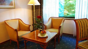 A room with two armchairs, a small table with a fruit bowl, a lamp, and a window with a view of greenery.