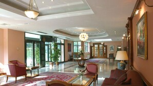A spacious lobby with a high ceiling, large windows, and a central seating area with a glass table. - Hotel AS (Zagreb)