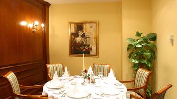 A dining room with a round table set for four, surrounded by striped chairs, a painting on the wall, and a large plant.