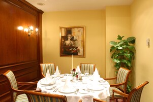 A dining room with a round table set for four, surrounded by striped chairs, a painting on the wall, and a large plant.