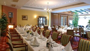 A formal dining room with multiple tables set for service, wooden chairs, and a chandelier. - Hotel AS (Zagreb)