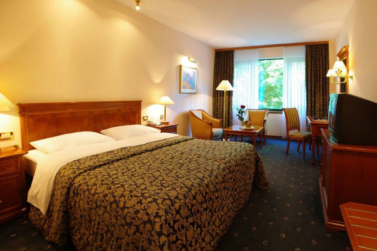 A hotel room with a large bed, two bedside tables, a desk with a chair, a television, and a window with curtains.