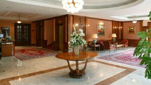 A lobby with a round table, a chandelier, a red carpet, and a large plant. - Hotel AS (Zagreb)