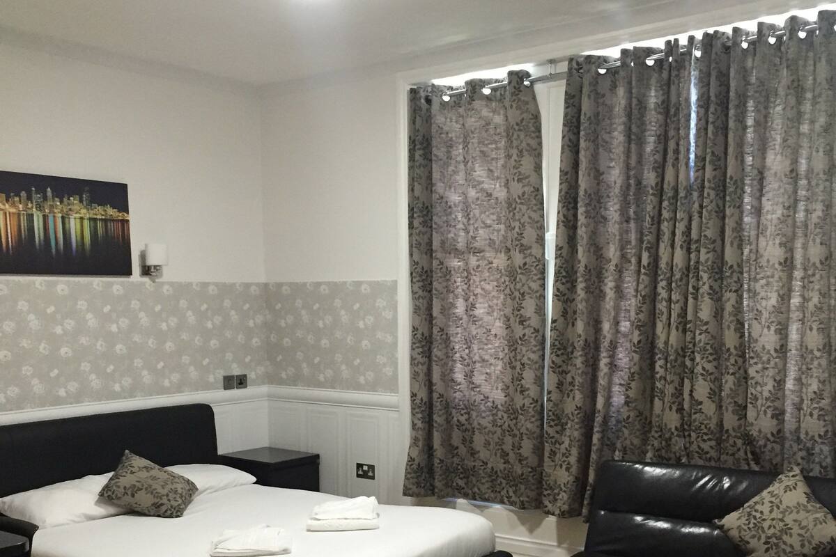 A hotel room with a bed, a sofa, a rug, and a painting on the wall.