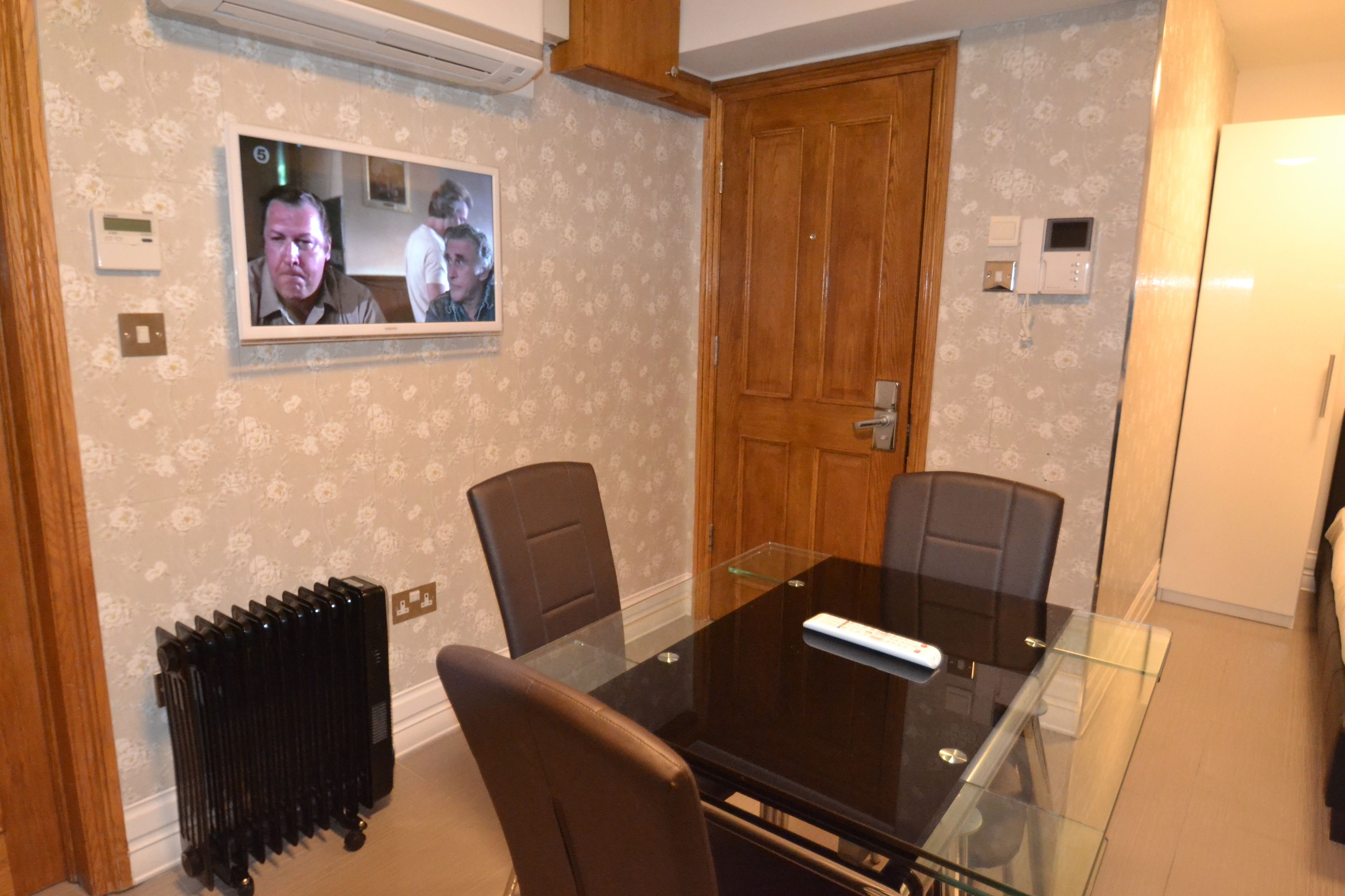 A conference room with a glass table, two chairs, a wooden door, and a wall-mounted television.