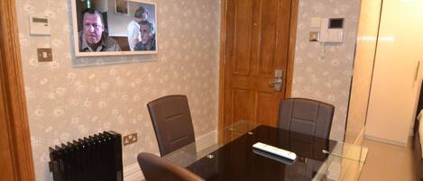 A conference room with a glass table, two chairs, a wooden door, and a wall-mounted television.