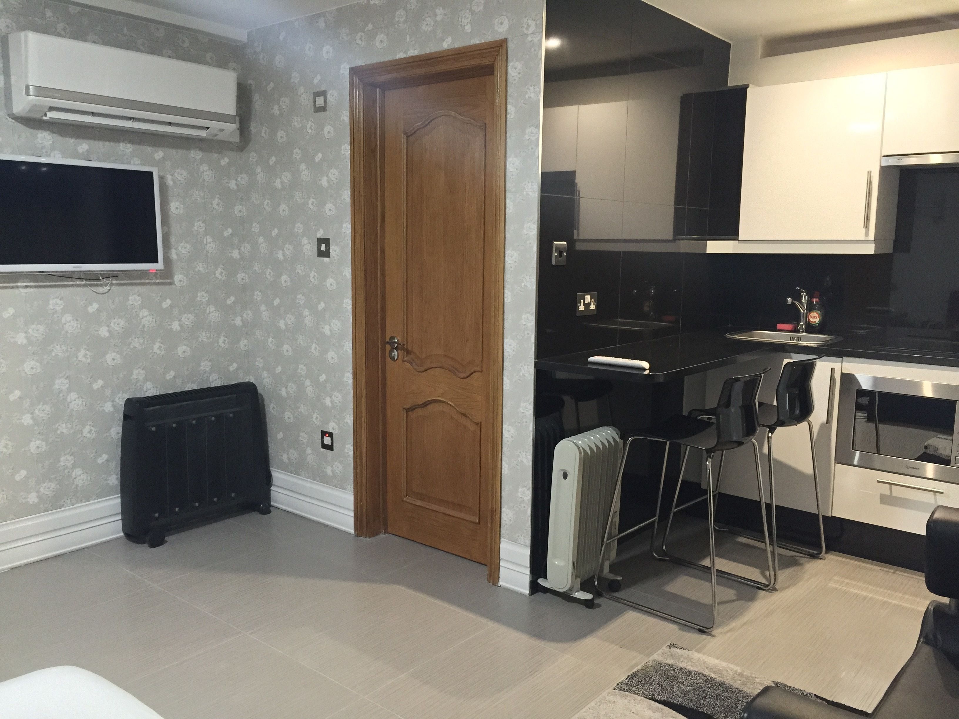A modern kitchen with a built-in oven, a microwave, and a sink. There is a wooden door leading to another room.