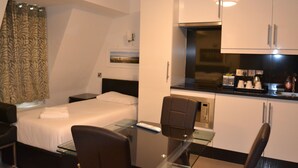 A hotel room with a bed, a desk with a chair, a kitchenette, and a bathroom. - Paddington Apartments (London)