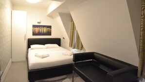 A bedroom with a bed, a black chair, a painting on the wall, and a window with curtains. - Paddington Apartments (London)