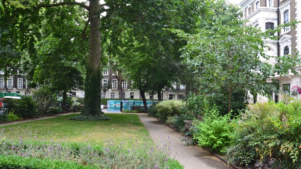 A pathway through a lush garden with mature trees and well-maintained hedges. - Paddington Apartments (London)