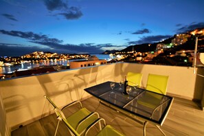 A balcony with a glass table and chairs, overlooking a cityscape at dusk. - Villa Rosa (Dubrovnik)