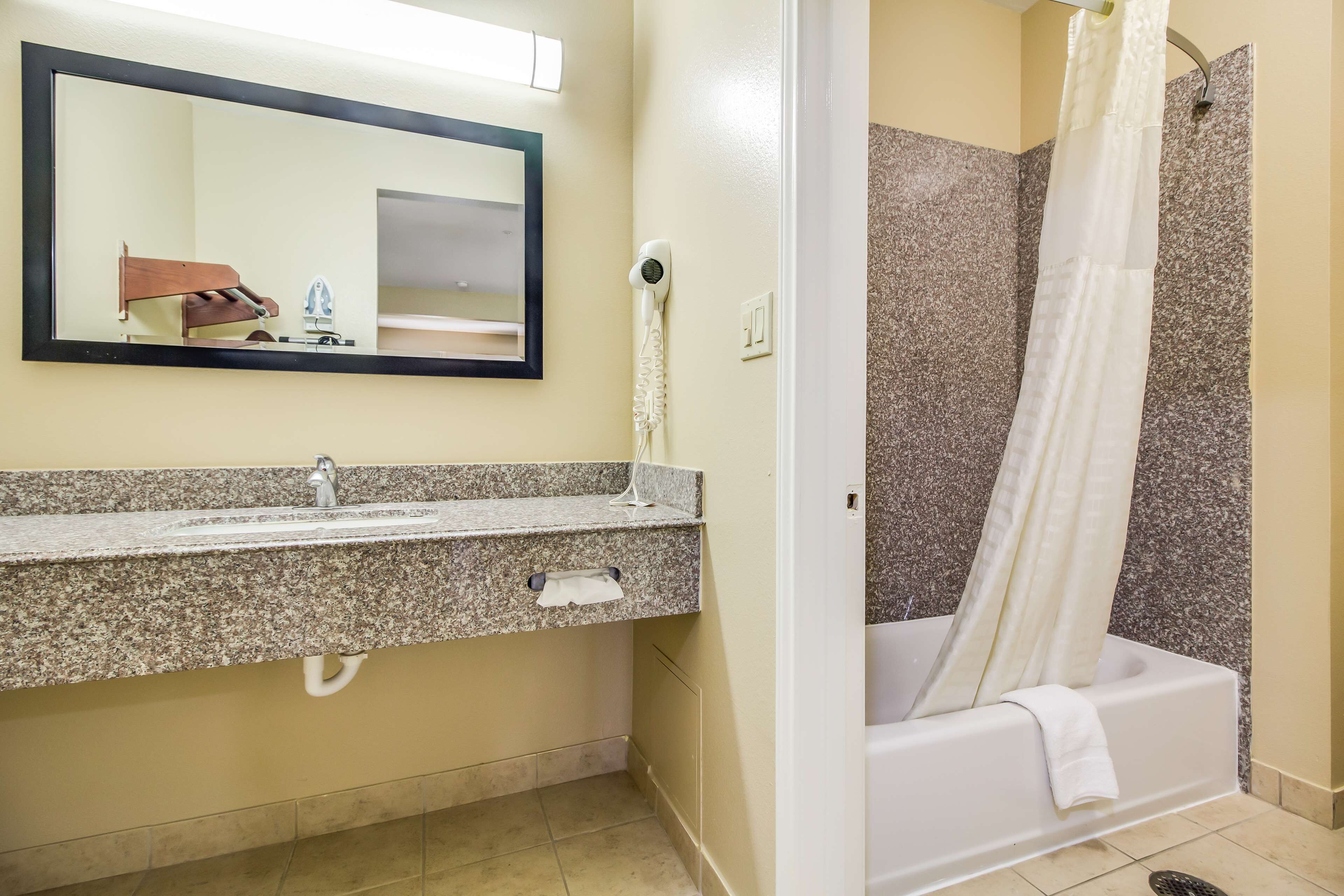 A bathroom with a granite countertop sink, a mirror, a hairdryer, and a shower with a white curtain.