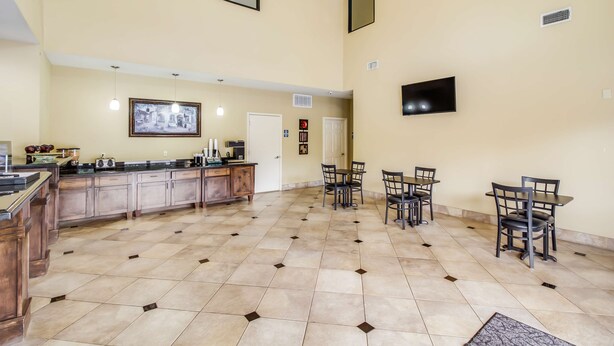A spacious kitchen with a tiled floor, wooden cabinets, a dining area with chairs and tables, a chandelier, and a flat-screen TV mounted on the wall.