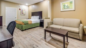 A hotel room with a bed, a sofa, a dining table, and a painting on the wall.