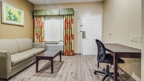 A room with a sofa, a small table, a chair, a door, and a window with curtains.