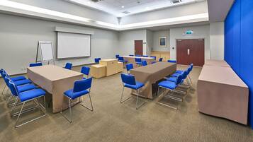 A conference room with beige tables and blue chairs, a whiteboard, and a projector screen.