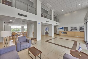 Un vestíbulo amplio con zonas de estar, un mostrador de recepción y vistas al exterior.