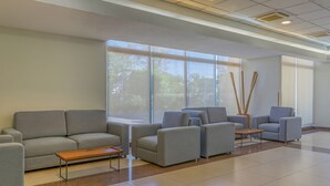 Un amplio vestíbulo con sofás grises, una mesa de centro de madera y ventanas grandes con vistas a árboles.