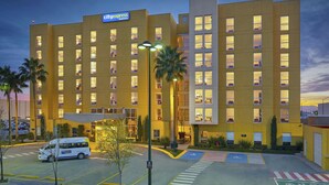 A hotel with a modern design, multiple floors, and a parking area with a bus.