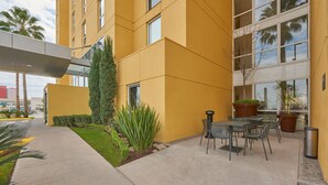 A modern building with a yellow facade, outdoor seating area, and a covered walkway.