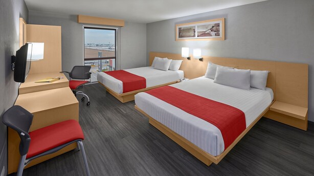A hotel room with two beds, a desk, a chair, a TV, and a window with a view.