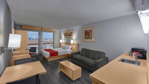 A hotel room with a bed, a sofa, a desk, a chair, a small table, and a sink.