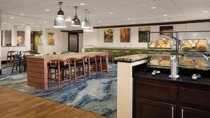 Un hall d’hôtel doté d’un bar central, de différents espaces aménagés pour s’asseoir et d’un buffet proposant des pâtisseries.