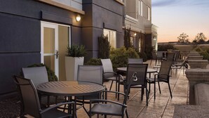 Une terrasse extérieure avec des tables et des chaises rondes, des plantes en pot et un bâtiment au design moderne.