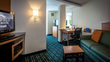 A hotel room with a television, a desk, a chair, a sofa, and a carpeted floor.