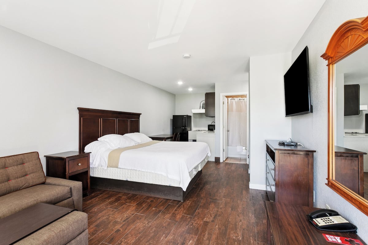 A hotel room with a bed, a sofa, a desk, a mirror, a TV, and a telephone.